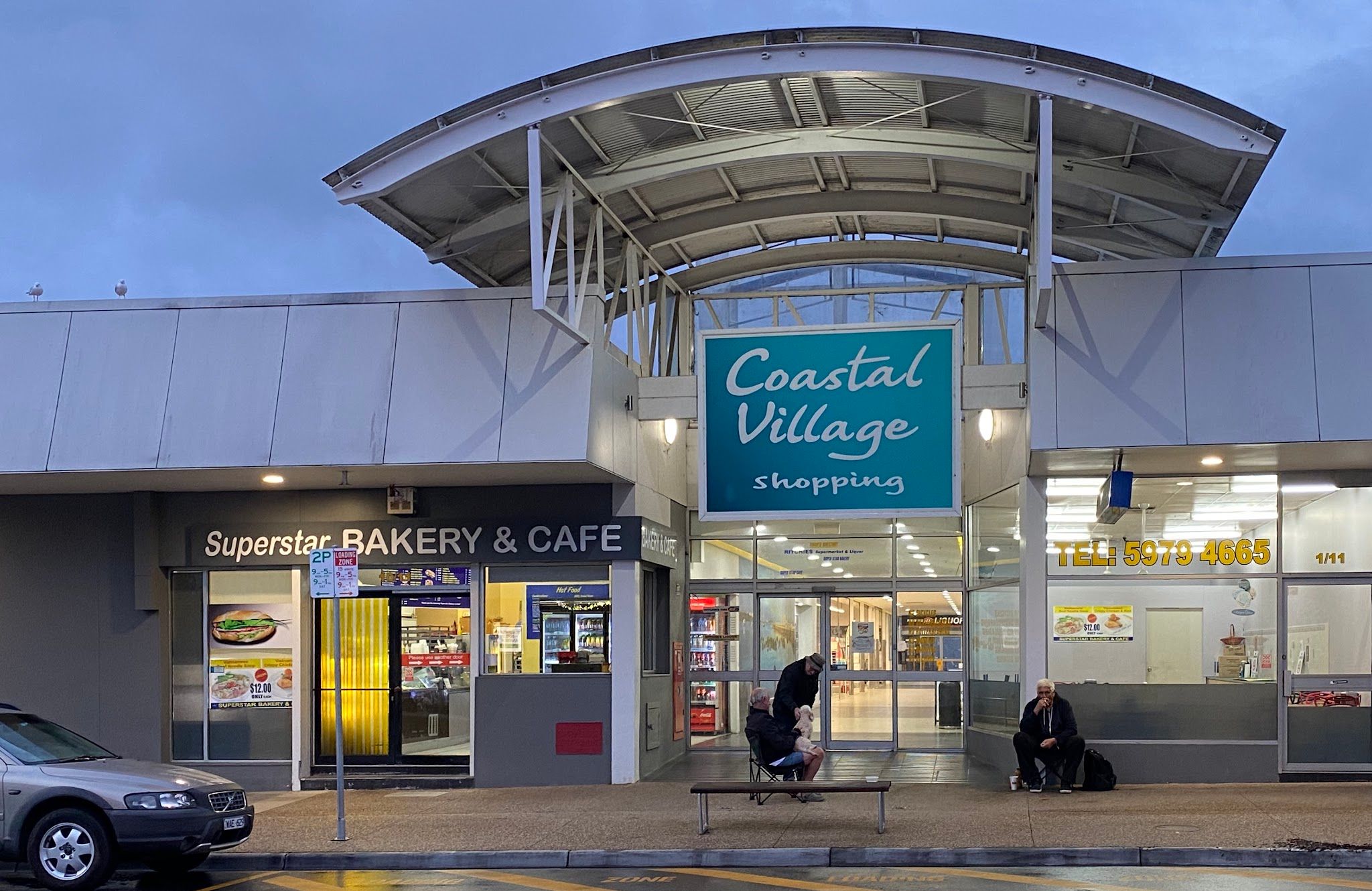 Superstar Bakery and Cafe shopfront at dusk, lit interior and signage visible at Coastal Village