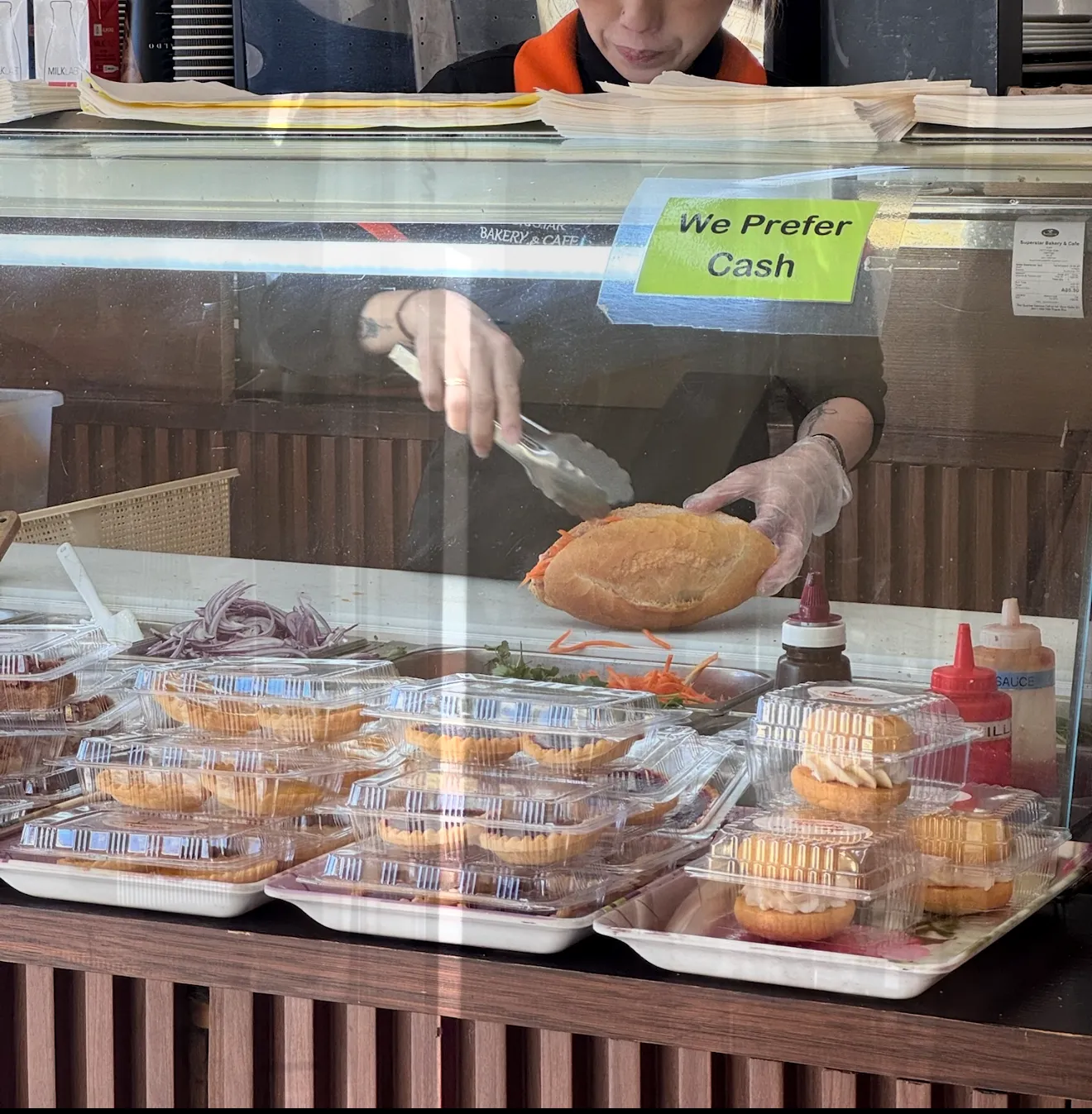 Staff member serving at the Superstar Bakery counter with pies and pastries on display
